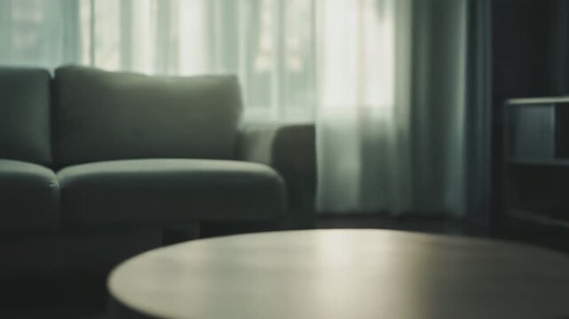 Circular wooden coffee table in focus, providing space for product display, with a blurred sofa and bright window in the background, creating a cozy and inviting home interior scene