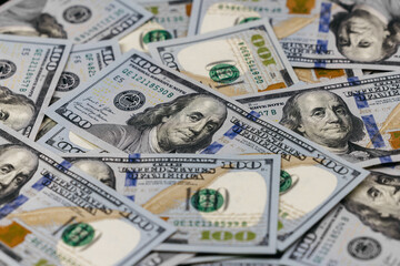 US dollar banknotes featuring Benjamin Franklin arranged in a scattered layout, showcasing intricate designs and security features on a flat surface