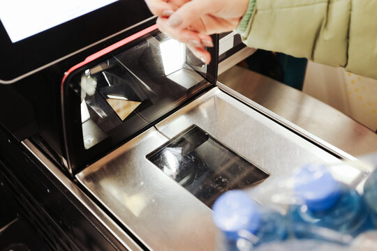 Customer scanning product at self checkout counter in grocery store. Barcode reader and payment terminal in use. Modern retail technology showing contactless shopping process at automated cashier.