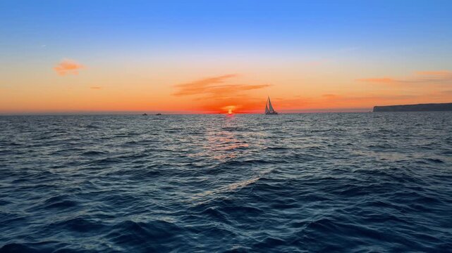 Sailboat silhouette at Mediterranean sunset over blue sea and horizon