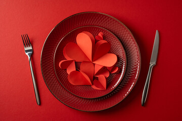 A romantic valentines table setting features a red heart on layered plates, polished cutlery and a...