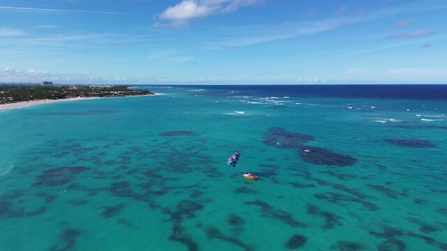 Aerial footage flyimg above turquoise sea following a speedboat towing a colorful parasail
