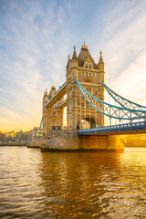 Obraz premium Tower Bridge stands majestically as the sun rises, casting warm hues over the Thames River. This iconic landmark is illuminated, showcasing its architectural beauty at dawn.