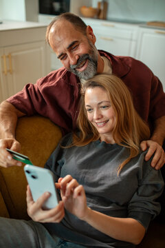 Smiling couple shopping online with credit card on sofa at home
