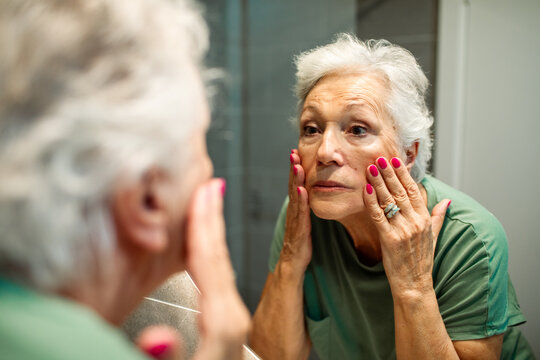 Senior woman examining her face in bathroom mirror