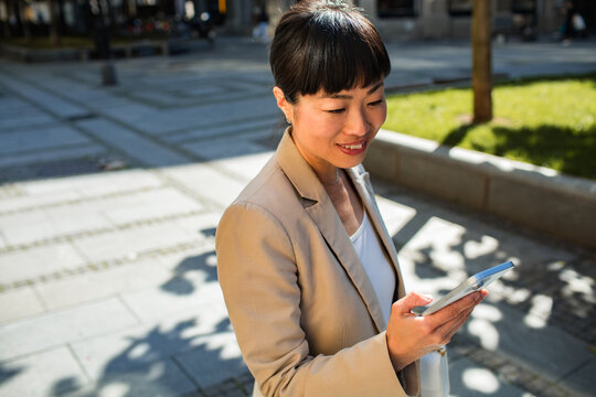 Smiling businesswoman using smartphone in sunny city plaza