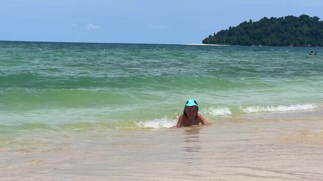 Landscapes of Manukan Island, which is part of the Tunku Abdul Rahman National Park in Sabah, Malaysia. Kota Kinabalu. A child is resting on white sand. A boy is swimming in turquoise water on a beach