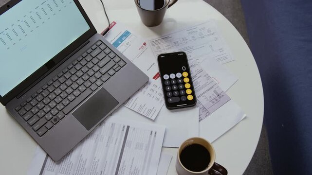 Top view close up shot of scattered financial documents on coffee table with open laptop and calculator, copy space