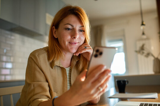 Smiling woman using smartphone in home kitchen