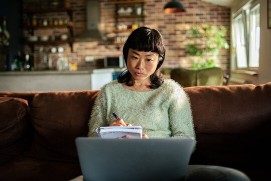 Woman studying with laptop on sofa at home