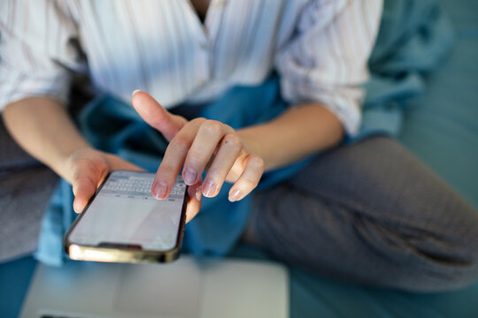Person typing on smartphone while sitting on bed at home