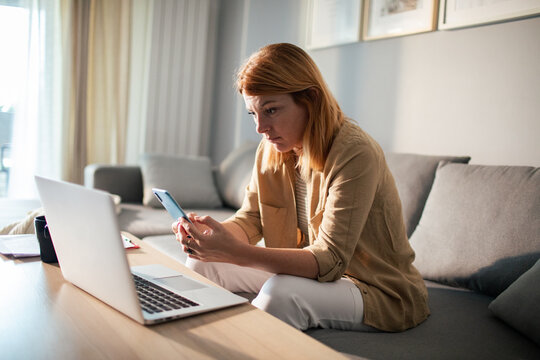 Woman checking smartphone while working from home on sofa