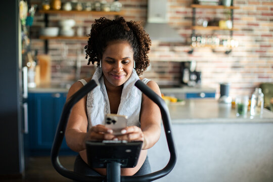 Woman using smartphone while cycling in home kitchen