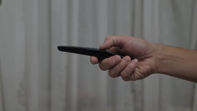 Casual evening remote interaction, Closeup of finger pressing remote button in cozy living room, Home entertainment scene showing person operating remote control against simple curtain background