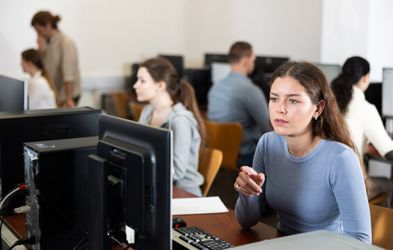 In group of students attending computer courses, female student attentively looks at monitor screen and does performs educational control work.