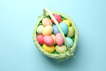 Fototapeta premium Easter basket with painted eggs on light blue background, top view