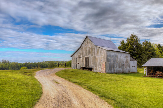 Rustic Barn on Country  Road.  A weathered barn sits beside a winding dirt path surrounded by lush green fields