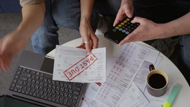 Top view close up shot of unrecognizable adult couple holding bills with past due notice and using calculator while doing budgeting together at home, copy space
