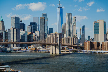 Naklejka premium View of Brooklyn Bridge and New York City skyline on a clear day. Brooklyn Bridge connects Manhattan and Brooklyn with tall buildings in the background under a blue sky.