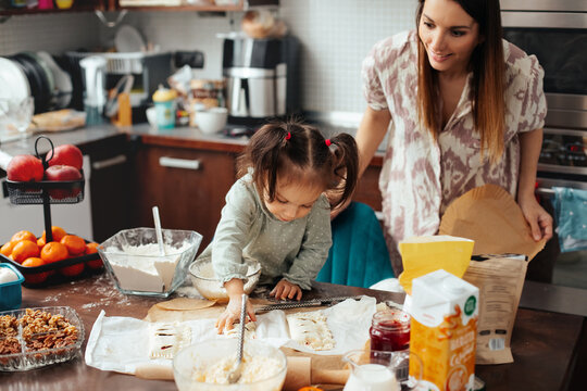Child and adult working together in kitchen making baked goods with ingredients and utensils scattered around during daytime