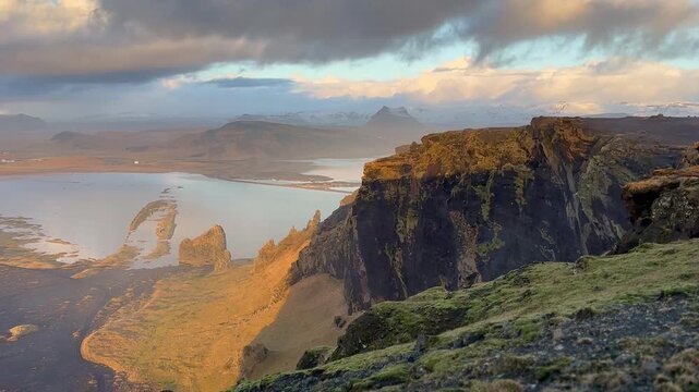 Static shot of sea cliffs and coastal lagoon with sunset sky reflections and winter grass, Dyrholaey, Iceland. HD 1080p.