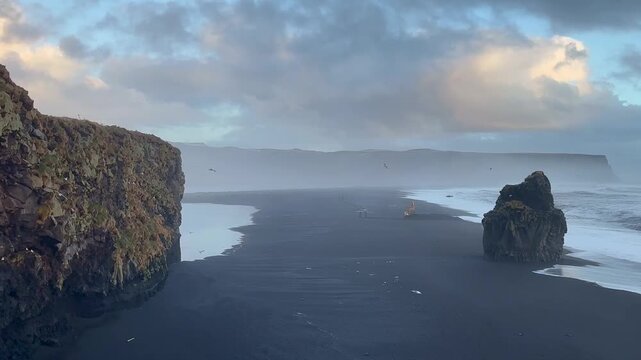 Wide static shot of Reynisfjara beach with distant excavator and seagulls under basalt cliffs, Iceland. HD 1080p.
