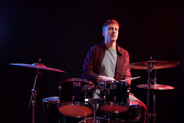 Man playing drums with drumsticks in color lights against black background