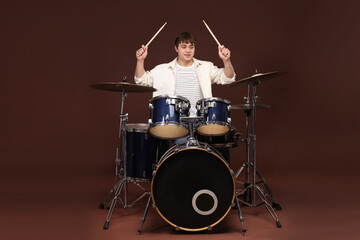 Smiling teenage boy with drumsticks learning how to play drums on brown background