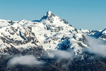 Aerial shot of snowcapped mountain peak above low clouds