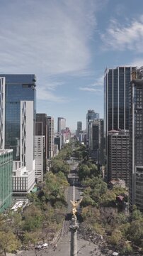 Aerial vertical view over Paseo de la Reforma during the Sunday ciclot&oacute;n as the drone flies backward revealing the Angel of Independence, surrounded by skyscrapers under a clear blue sky.