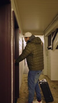 Adult man walking alone through outdoor motel corridor at night, carrying bag and returning to room. Travel lifestyle scene, road trip stop, temporary accommodation, solitude, evening routine.