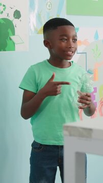 Vertical video: Poster cueing pupil in tee in class pointing, talking, tossing bottle in PAPER bin