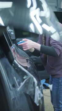 Professional detailer installing Paint Protection Film (PPF) on car B-pillar. Close-up of hands using squeegee and knife to apply transparent anti-gravel vinyl.
