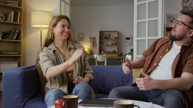 Front view shot of adult couple closing laptop and celebrating with high five after finishing filing taxes or planning budget at home together
