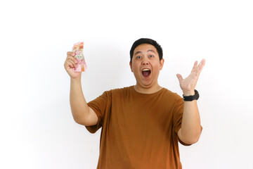 An Indonesian Asian man holds money, cheering and expressing excitement about good news or a...