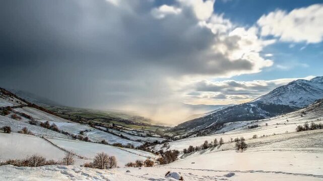 A serene landscape of rolling hills and mountains under a partly cloudy sky with patches of snow and autumn foliage
