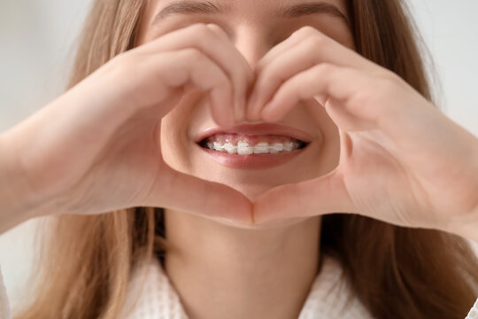 Smiling young woman with dental braces making heart gesture in bathroom, closeup