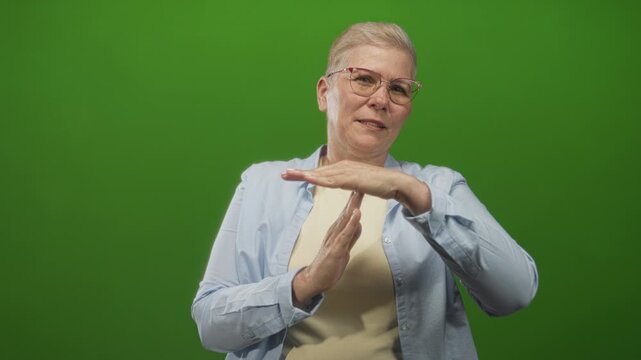 Woman with hands forming a time out gesture in a green studio setting, wearing glasses and casual shirt; assertive boundary confidence.