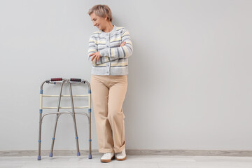 Mature woman with walker near light wall