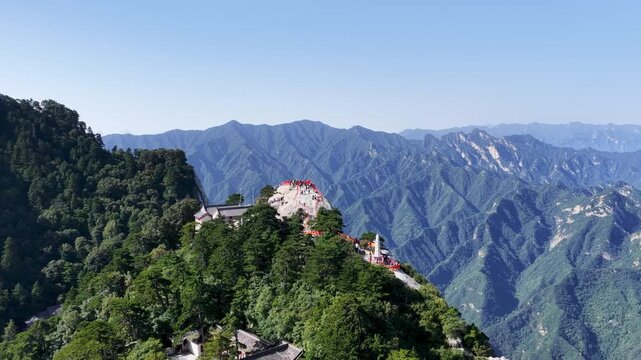 Aerial drone footage of the West Peak at Mount Hua, lush green mountains, ancient temple, and hikers on a winding path, retreating wide-angle perspective, China
