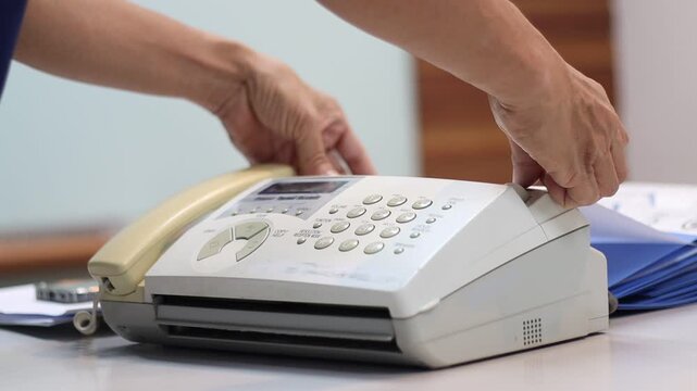 A man hands using a fax machine, placing paper into the tray and sending a fax in an office