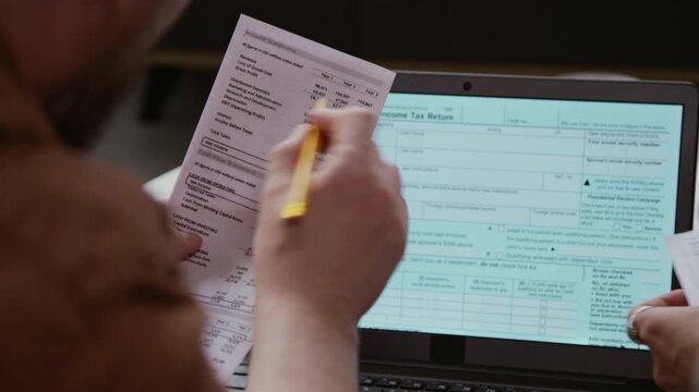 Over shoulder close up shot of unrecognizable adult couple filling online tax forms and holding financial documents while working with finances, copy space