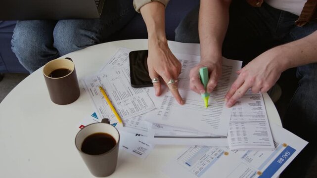 Top view close up shot of unrecognizable couple managing home finances together with man highlighting lines in document, copy space