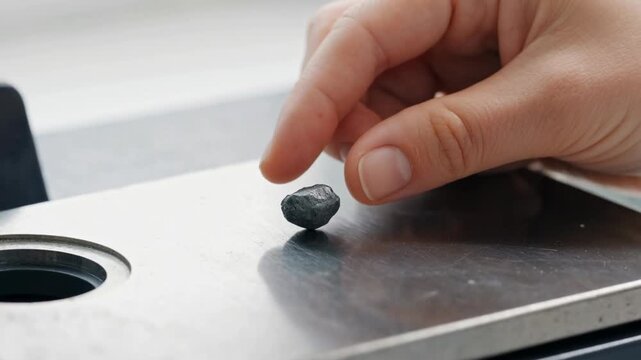 Critical mineral resources geology rock ore sample inspection metal surface laboratory table human hand holding raw mineral object scientific research science lab analysis mining industry natural