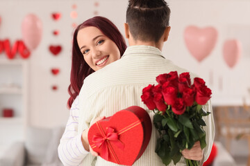 Young lovely couple with bouquet of roses and gift hugging at home. Valentine's Day celebration