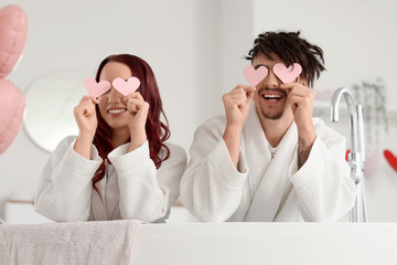 Young lovely couple with paper hearts sitting in bathtub at home. Valentine's Day celebration
