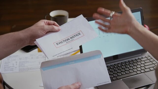 Top view close up shot of man opening envelope getting eviction notice while unrecognizable couple sorting mail and managing home finances, focus on hands over table