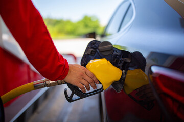 Naklejka premium A person refueling a car at a gas station with a yellow fuel nozzle inserted into the vehicle's fuel tank