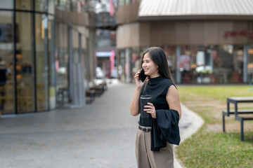 Fototapeta premium Asian woman smiling talking on phone holding coffee