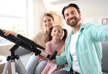 Fototapeta premium Little girl and her parents with telescope taking selfie on sofa at home
